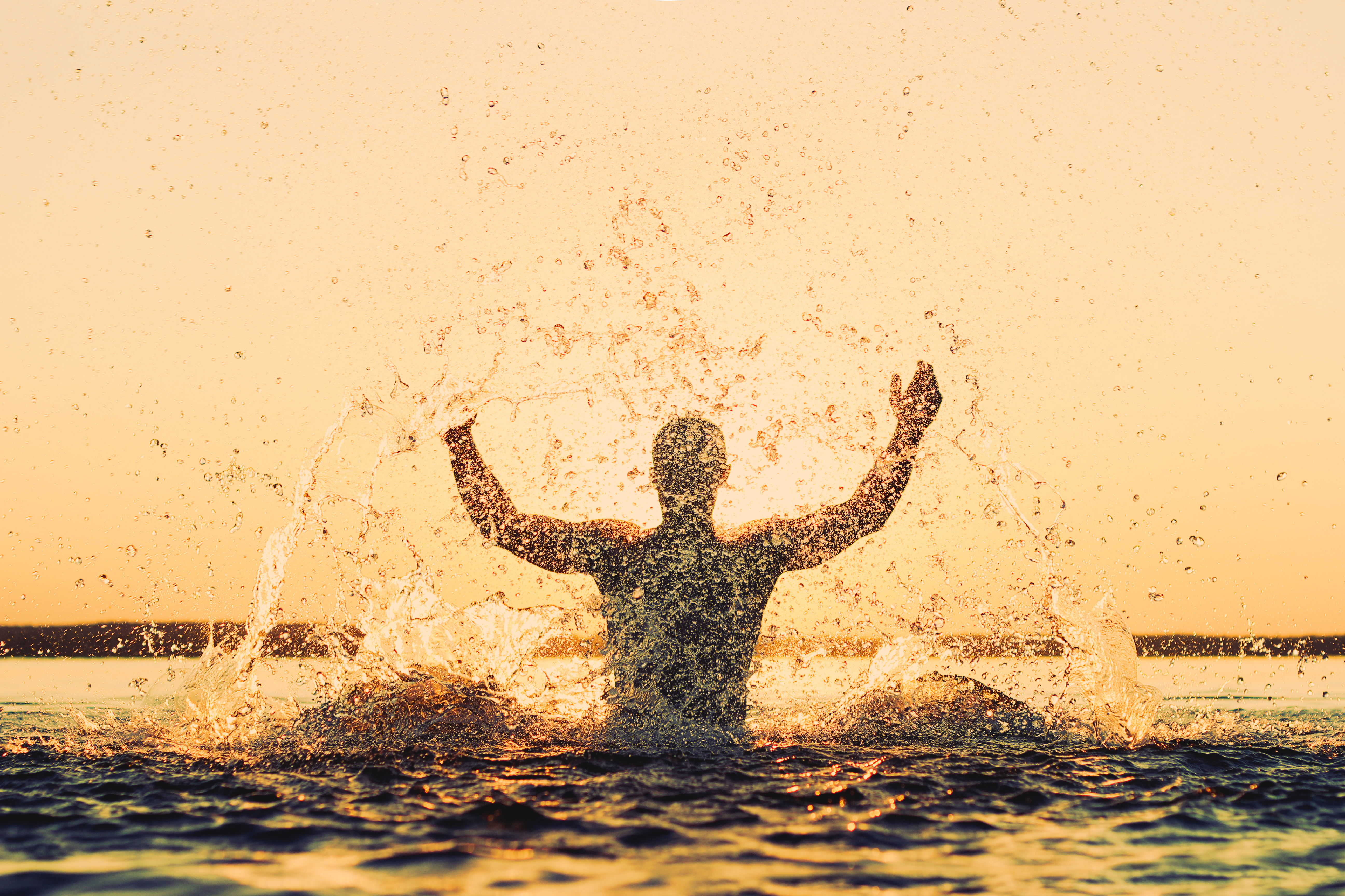 a person waist deep in the sea splashing water at sunset